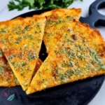 Crisp keto garlic bread triangles topped with garlic butter and parsley on a black serving skillet.