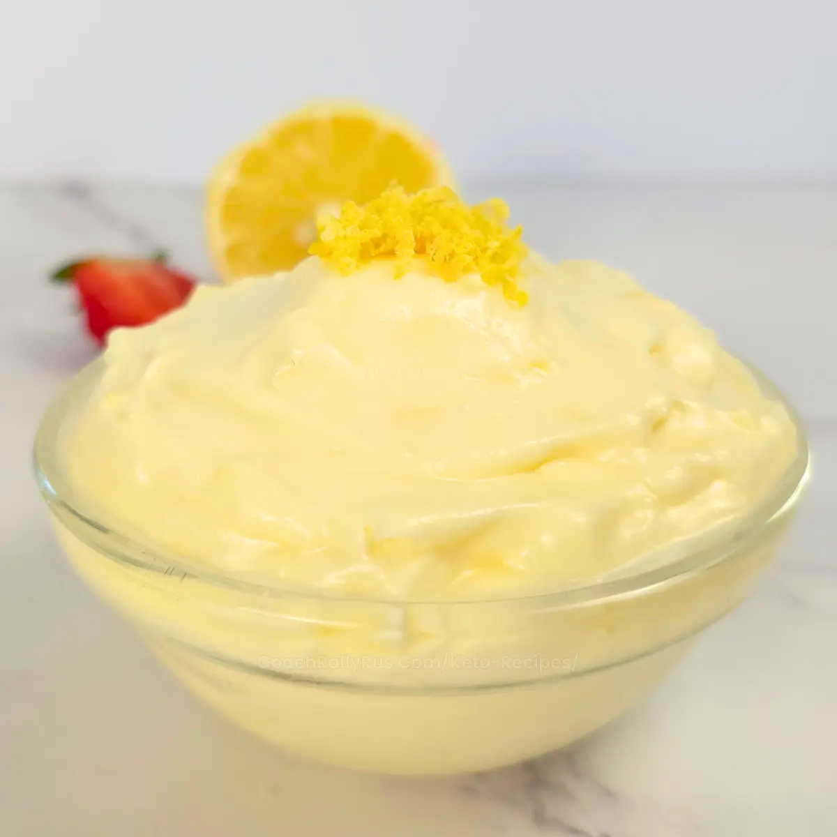 Keto lemon cheesecake fluff in a bowl with strawberry and lemon Close up of keto lemon cheesecake fluff topped with fresh lemon zest