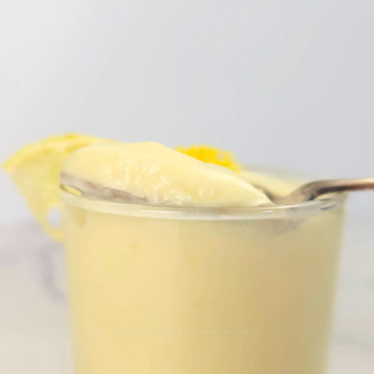 Keto lemon mousse topped with zest and lemon wedge, spoon resting inside.