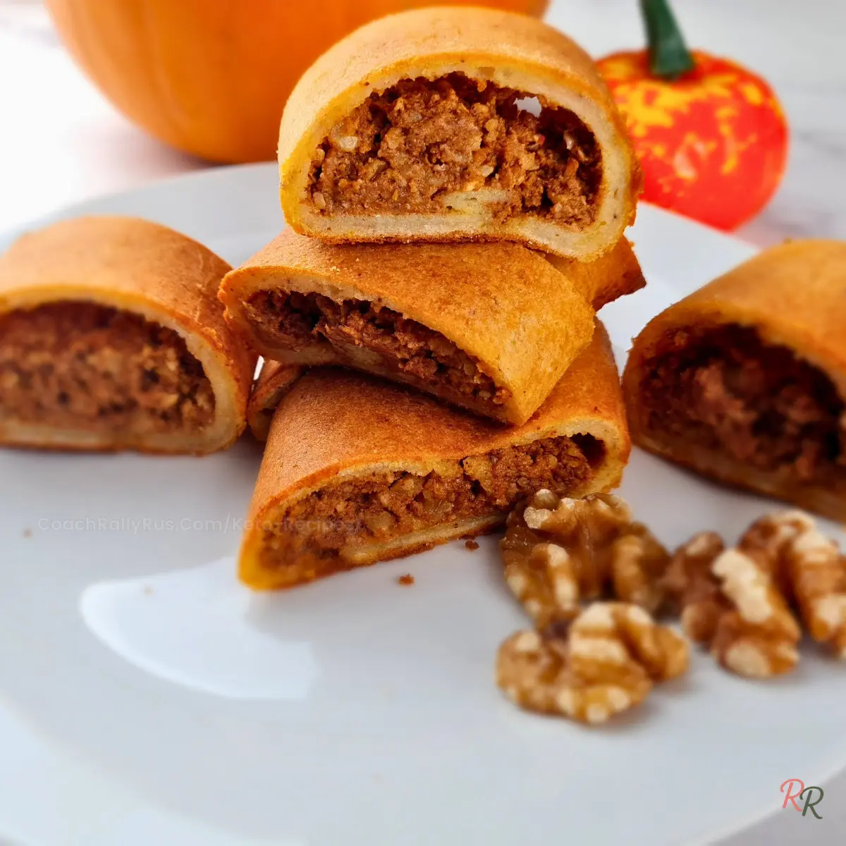 Keto pumpkin pinwheels stacked on a plate with walnuts and cinnamon