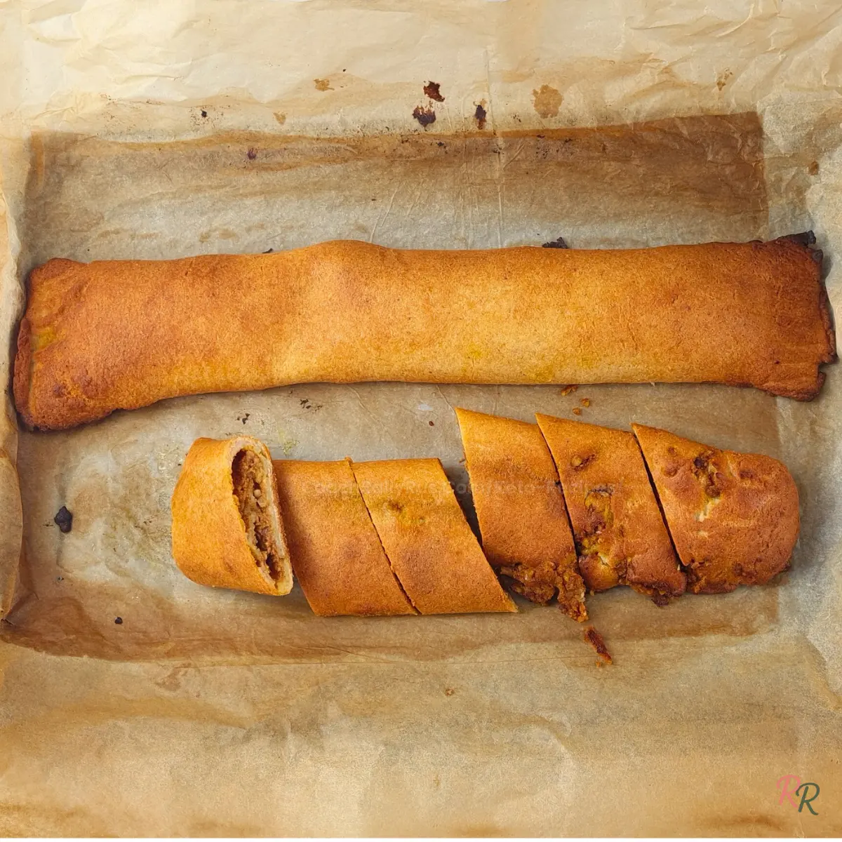 Sliced baked keto pumpkin pinwheel log on parchment paper, showing golden crust and nutty pumpkin filling