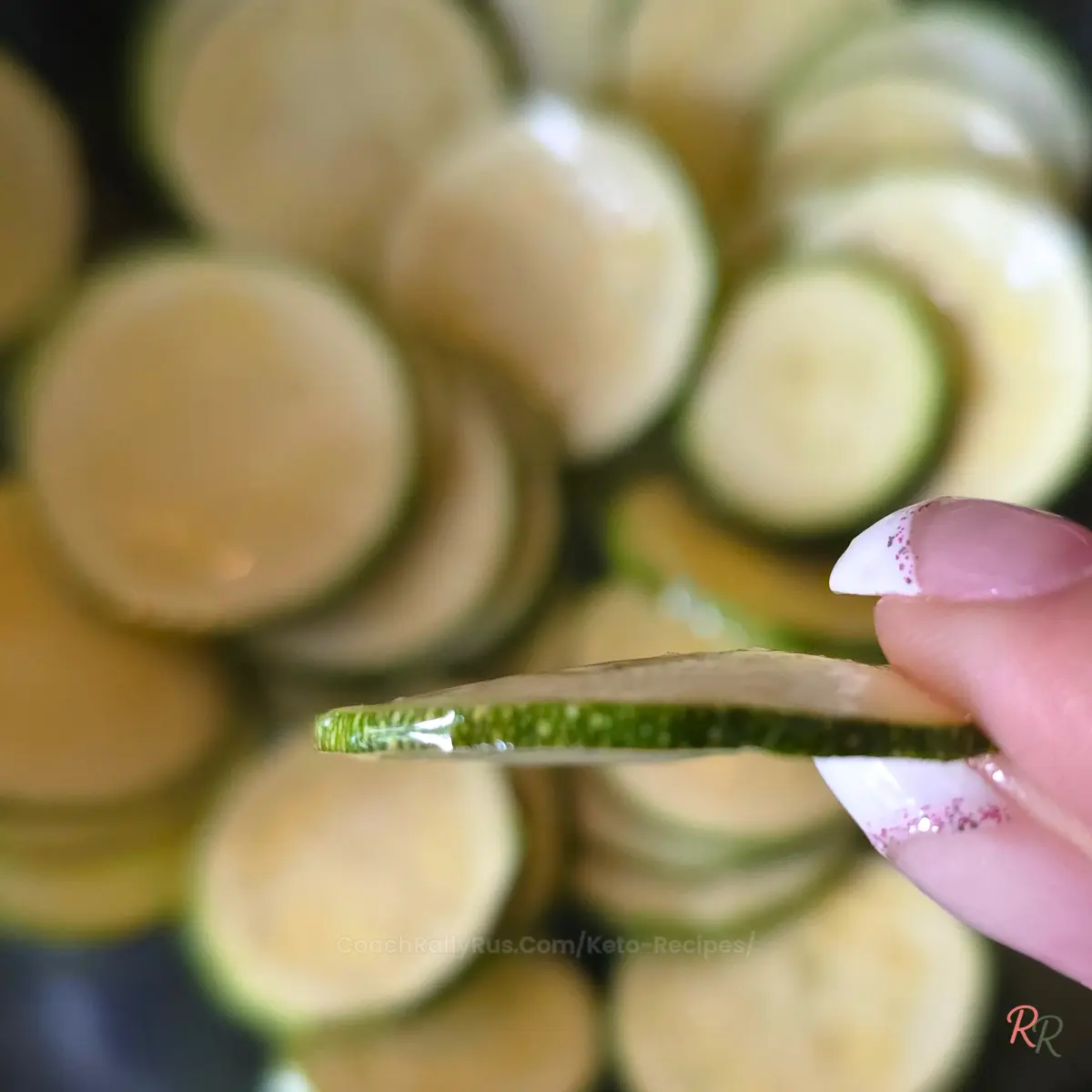 Close-up of a single thin zucchini slice held between fingers to show ideal thickness