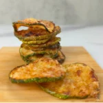 Stack of golden brown keto zucchini chips on a wooden board