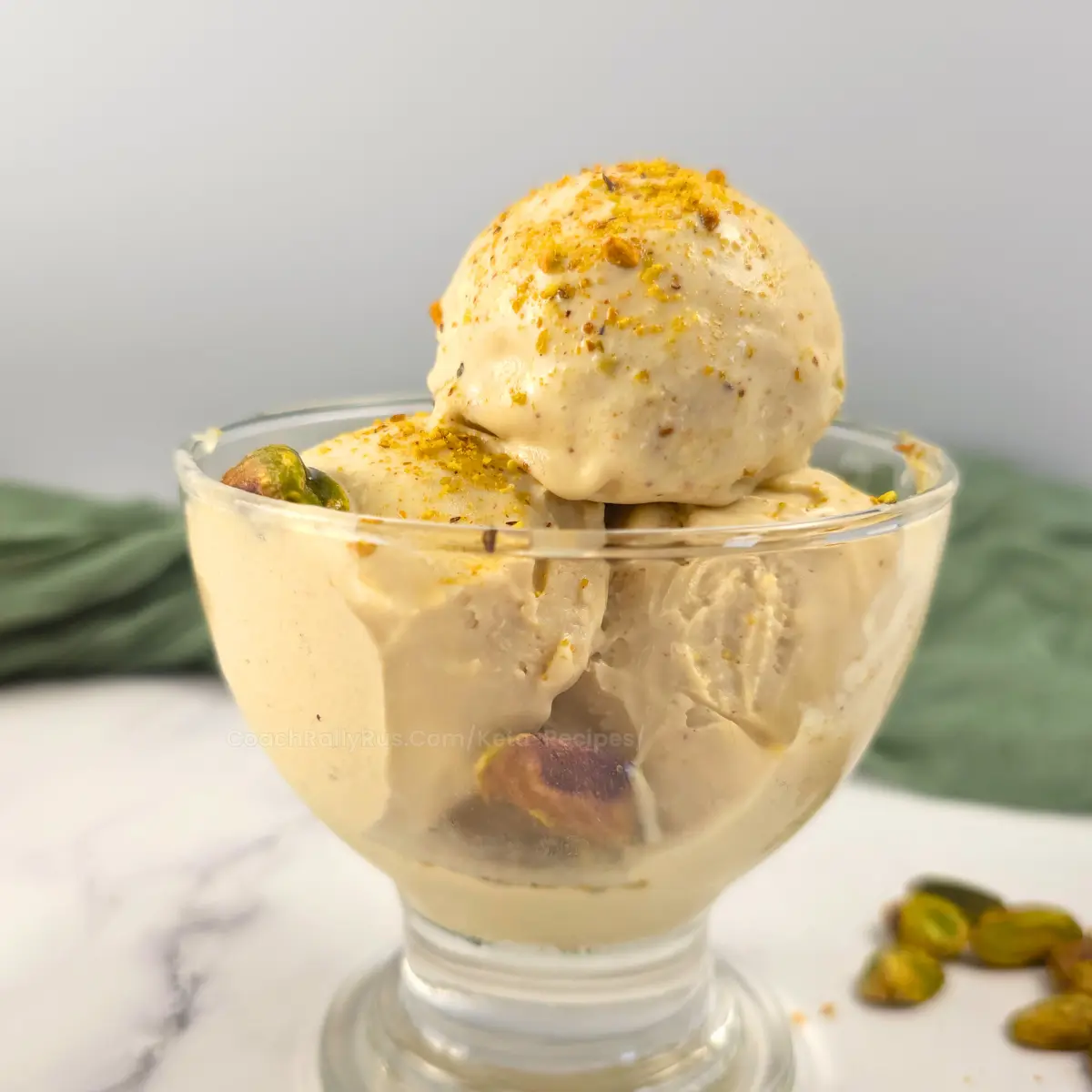 Three scoops of pistachio cottage cheese ice cream in a glass bowl, dusted with pistachio crumbs.