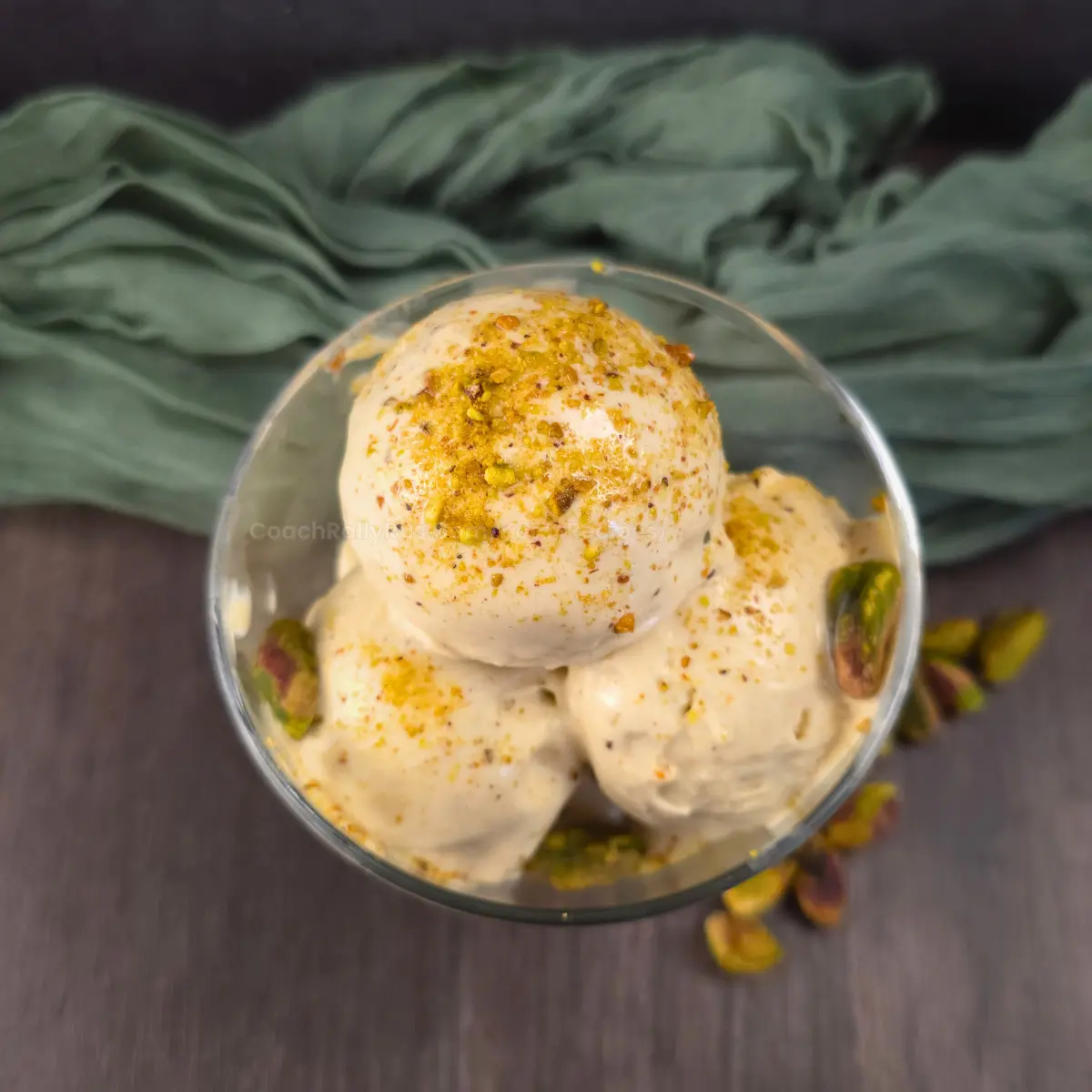 Overhead shot of keto pistachio ice cream in a glass dessert bowl on a dark wood table.