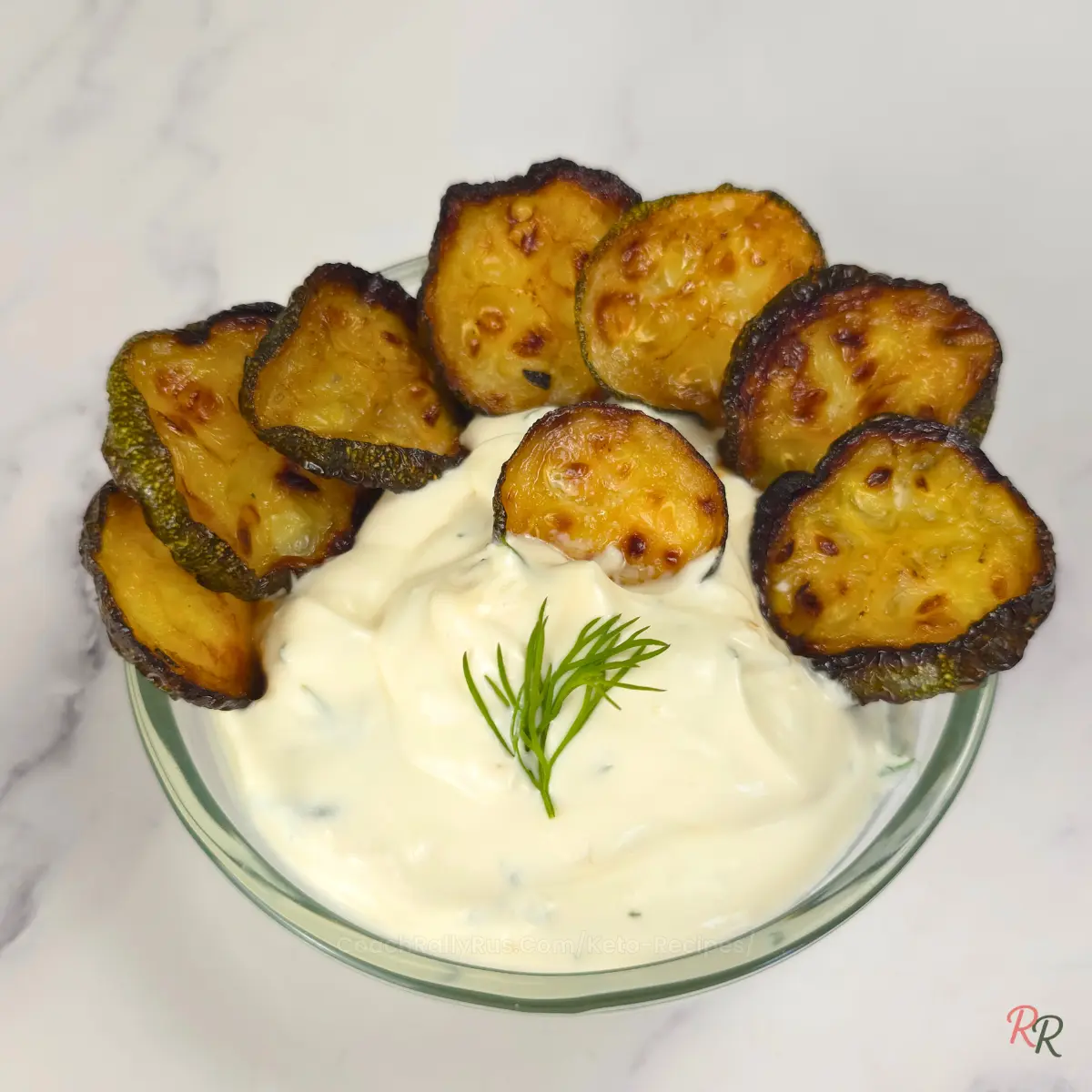 Creamy yogurt dip with roasted zucchini rounds and dill, styled in a bowl with garlic in background