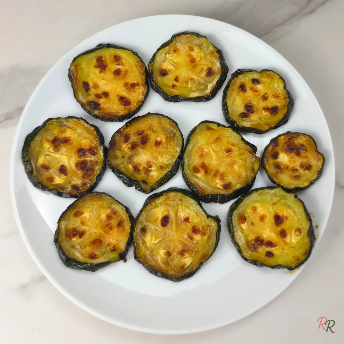 Plain roasted zucchini slices with golden tops on a white plate, no sauce.