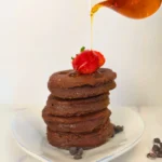 Stack of thick chocolate keto pancakes topped with syrup and fresh strawberry