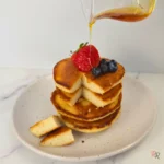 Stack of almond flour pancakes topped with berries and syrup being poured over them