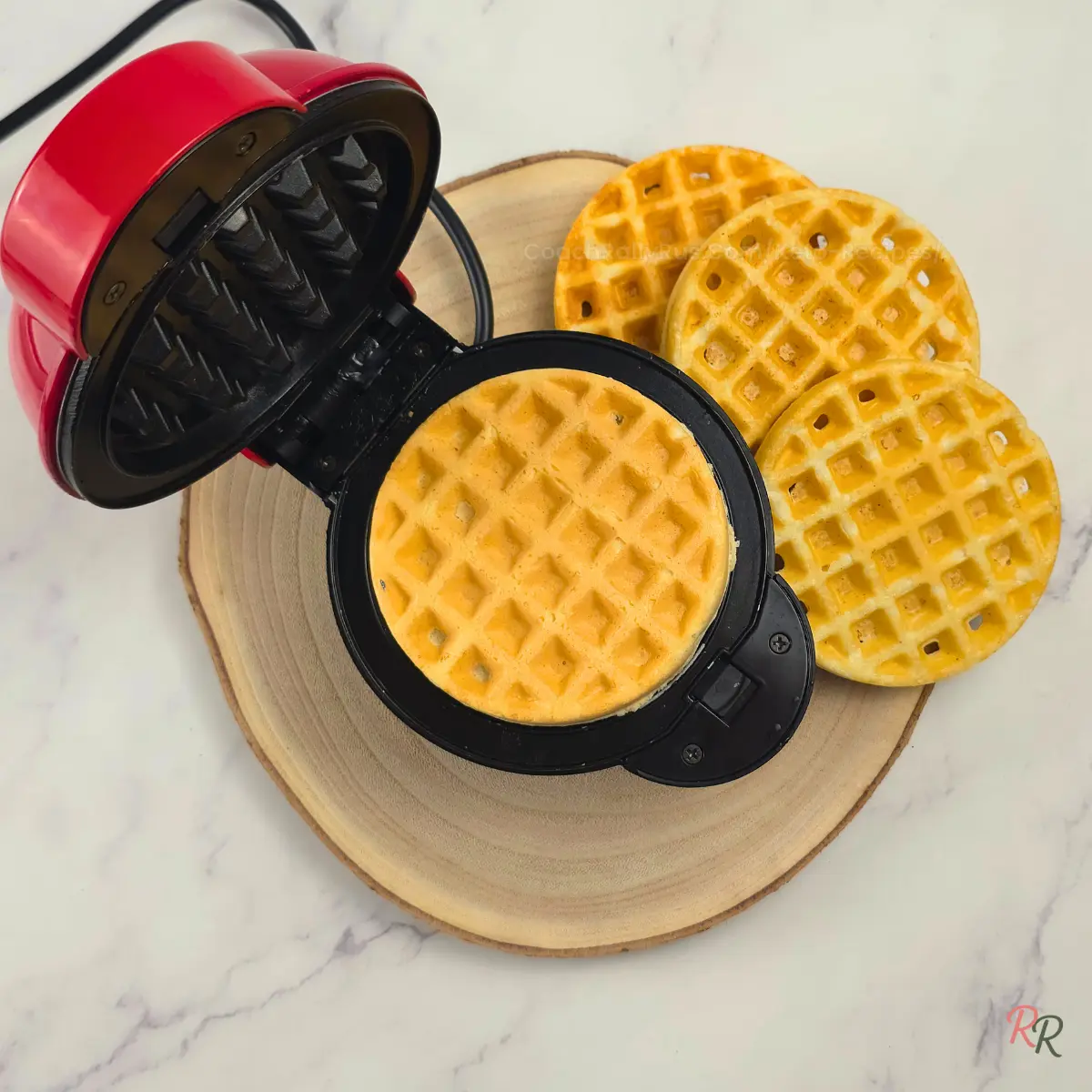 Mini waffle maker cooking keto almond flour waffle with finished waffles in the background