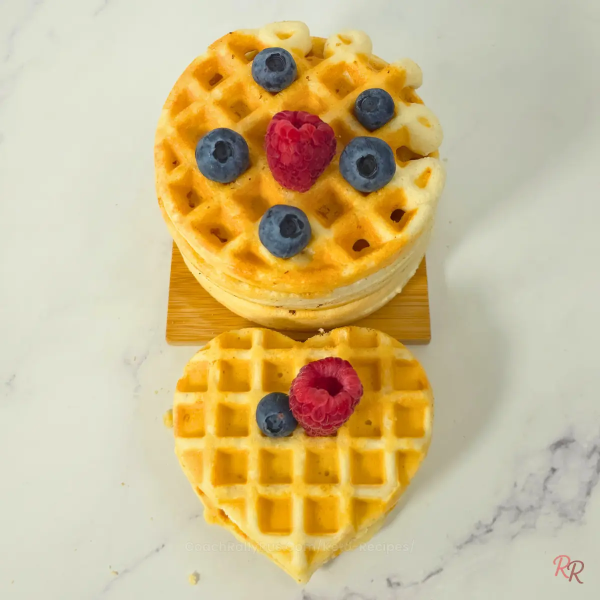 Stack of almond flour waffles topped with raspberries and blueberries, next to a heart-shaped waffle