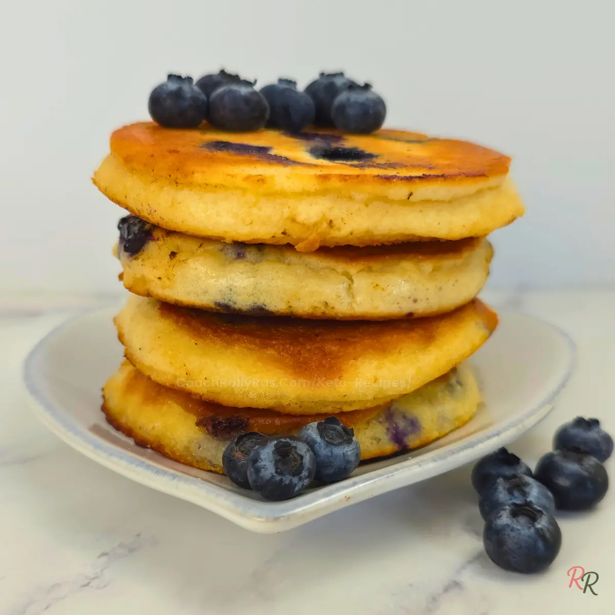 Keto blueberry pancakes with syrup and fresh blueberries on a plate