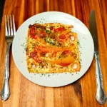 Keto chaffle pizza topped with cheese, pepperoni, and herbs on a wooden board.