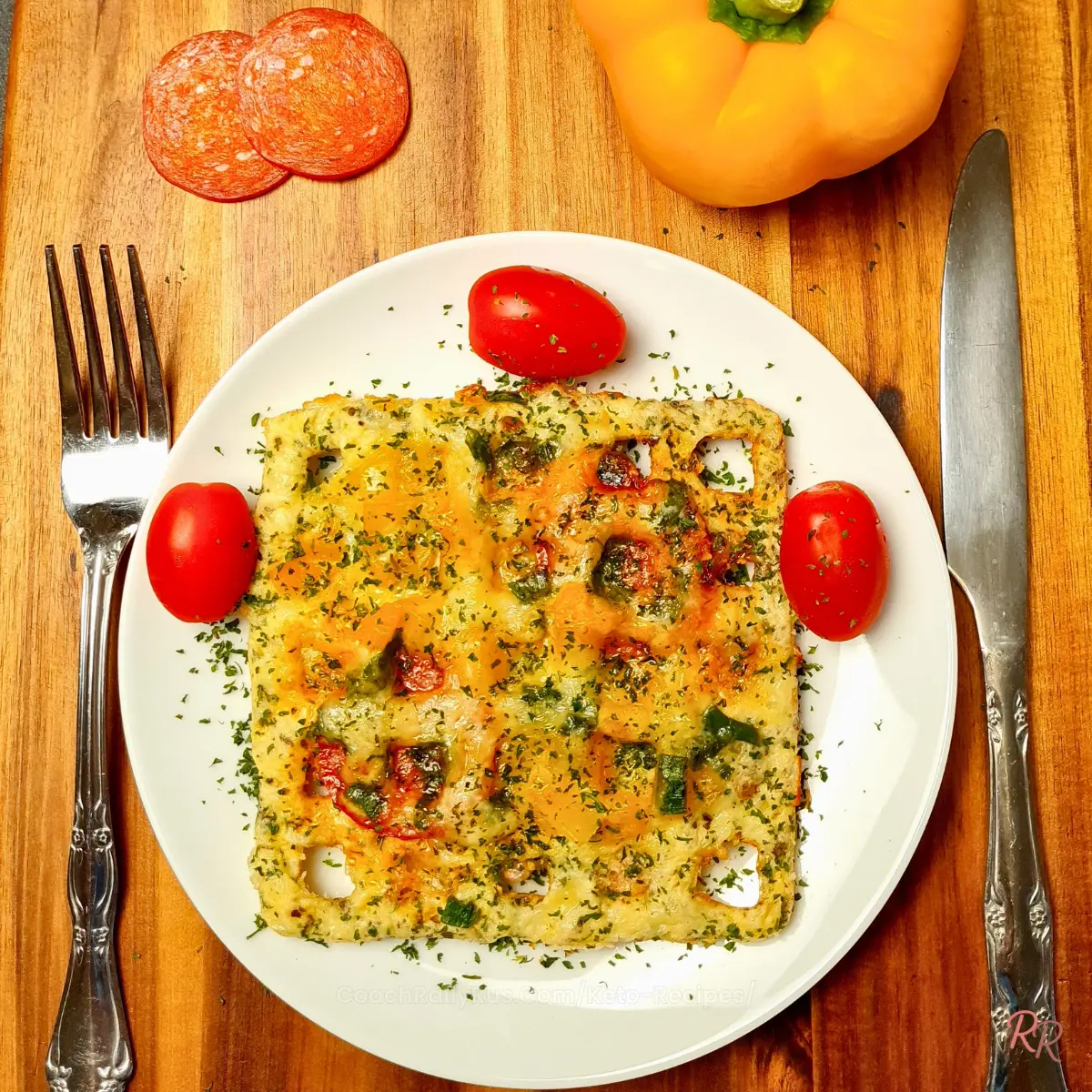 Keto chaffle pizza on a plate with cherry tomatoes and pepperoni slices on the side.