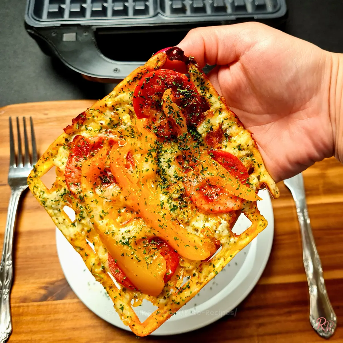 Hand holding a slice of crispy keto chaffle pizza with pepperoni and peppers.