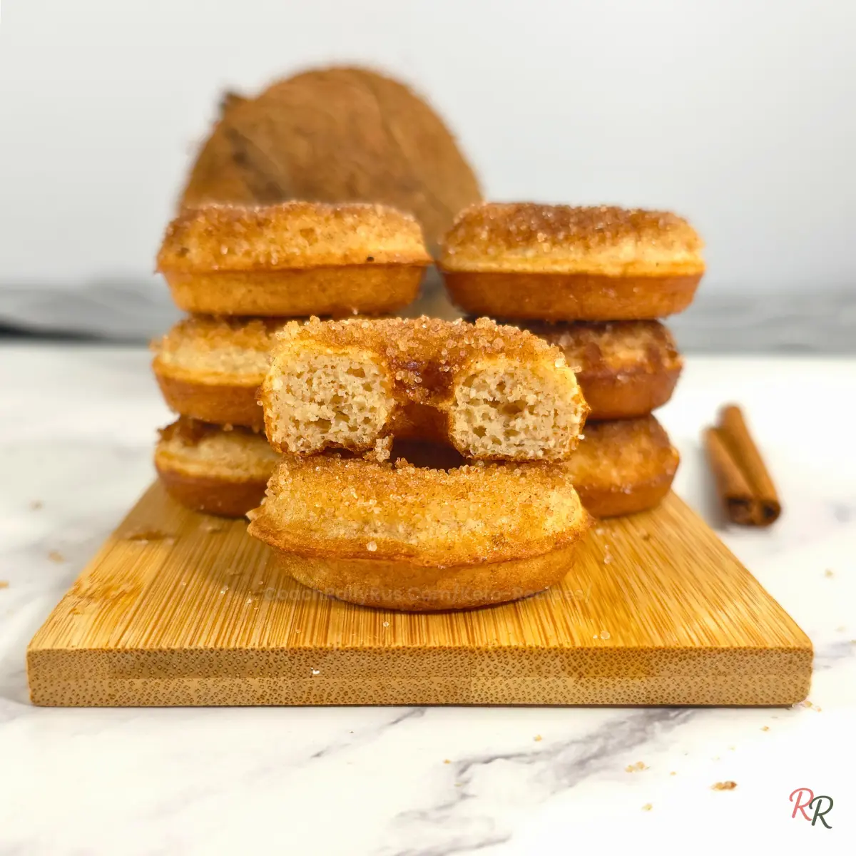 Stack of keto cinnamon sugar cottage cheese donuts made with coconut flour, with one sliced donut showing the fluffy inside.