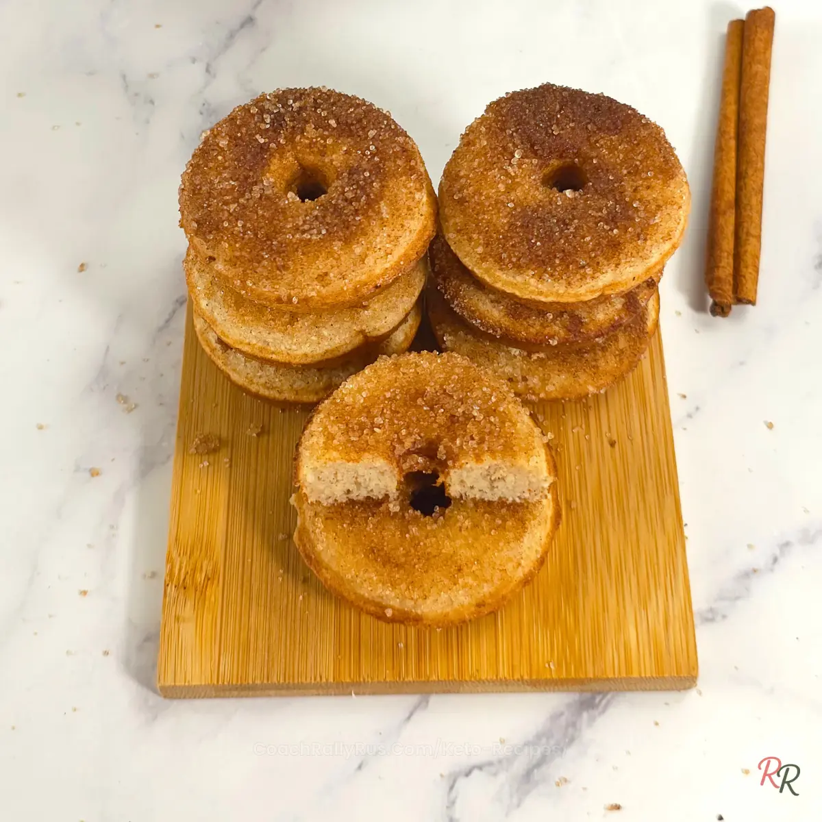 Overhead view of stacked keto cinnamon donuts on a wooden board with cinnamon sticks.