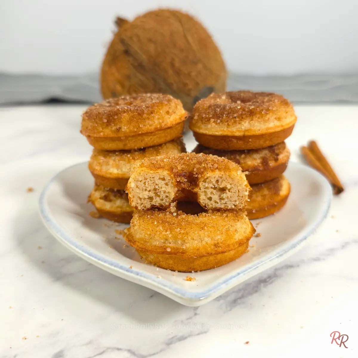 Golden keto donuts stacked on a wooden board with one donut cut in half to show soft, airy texture.