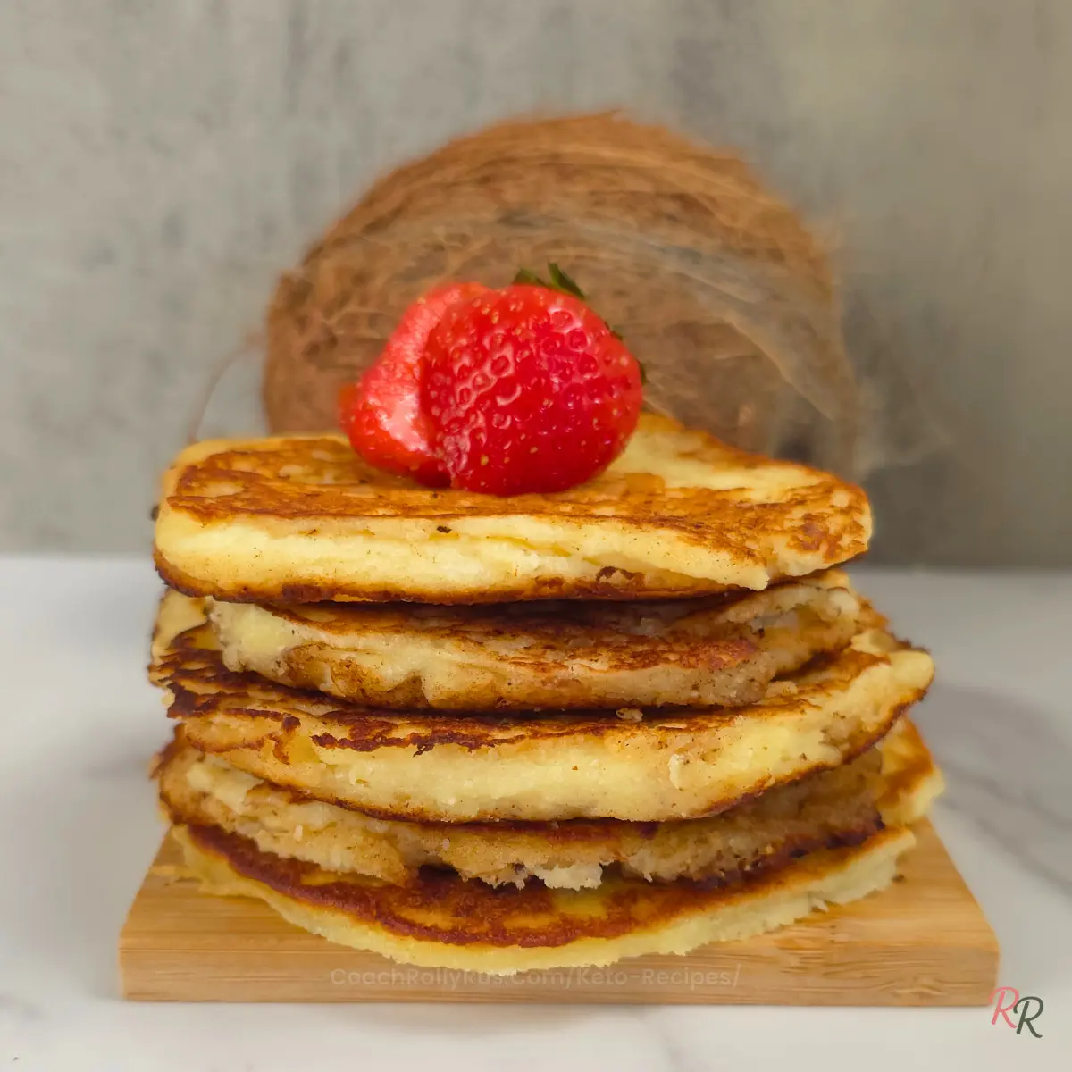 Tall stack of keto coconut pancakes with a whole strawberry and coconut