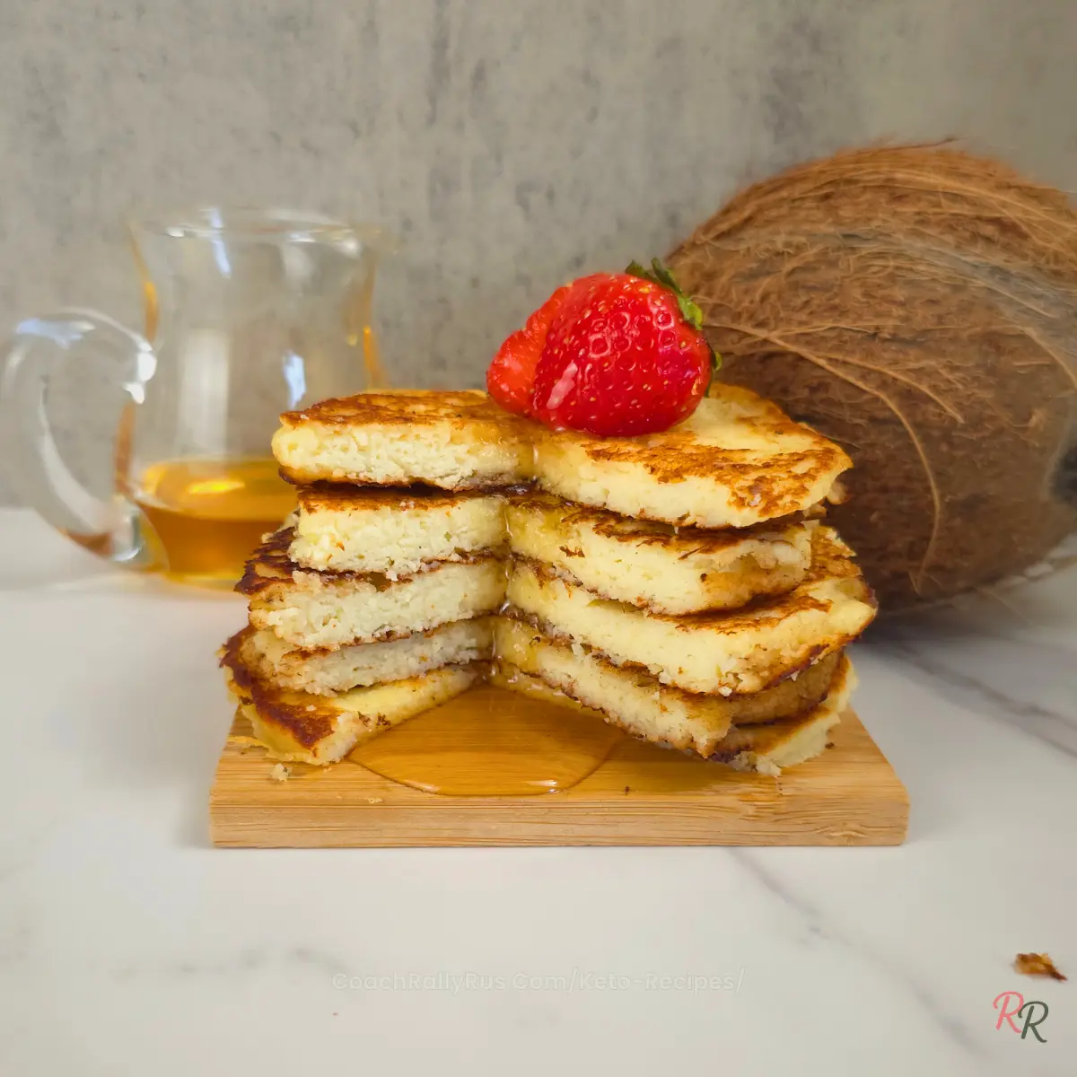 Stack of fluffy keto coconut flour pancakes with syrup and a strawberry on top