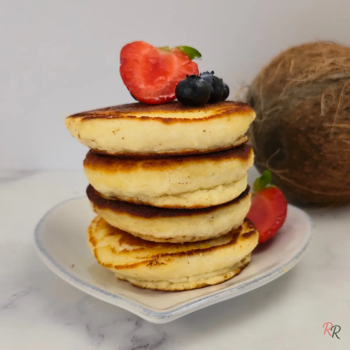Stack of golden keto coconut flour pancakes topped with strawberries and blueberries