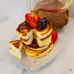 Syrup being poured over a stack of keto coconut flour pancakes with strawberries and blueberries