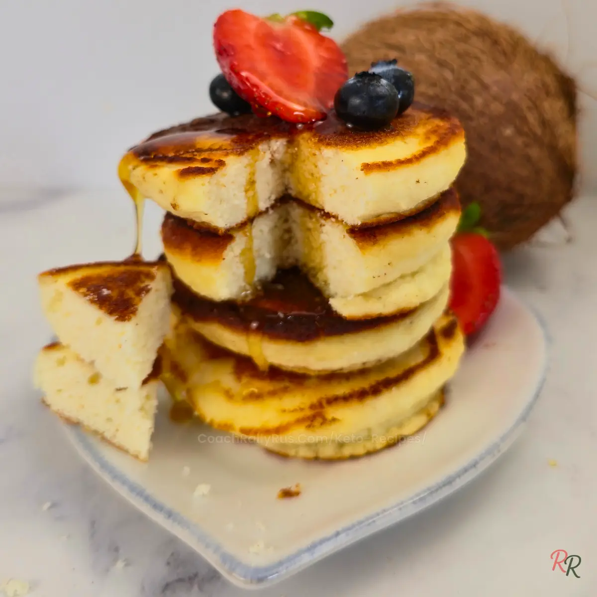 Closeup of sliced keto coconut pancakes with berries and syrup
