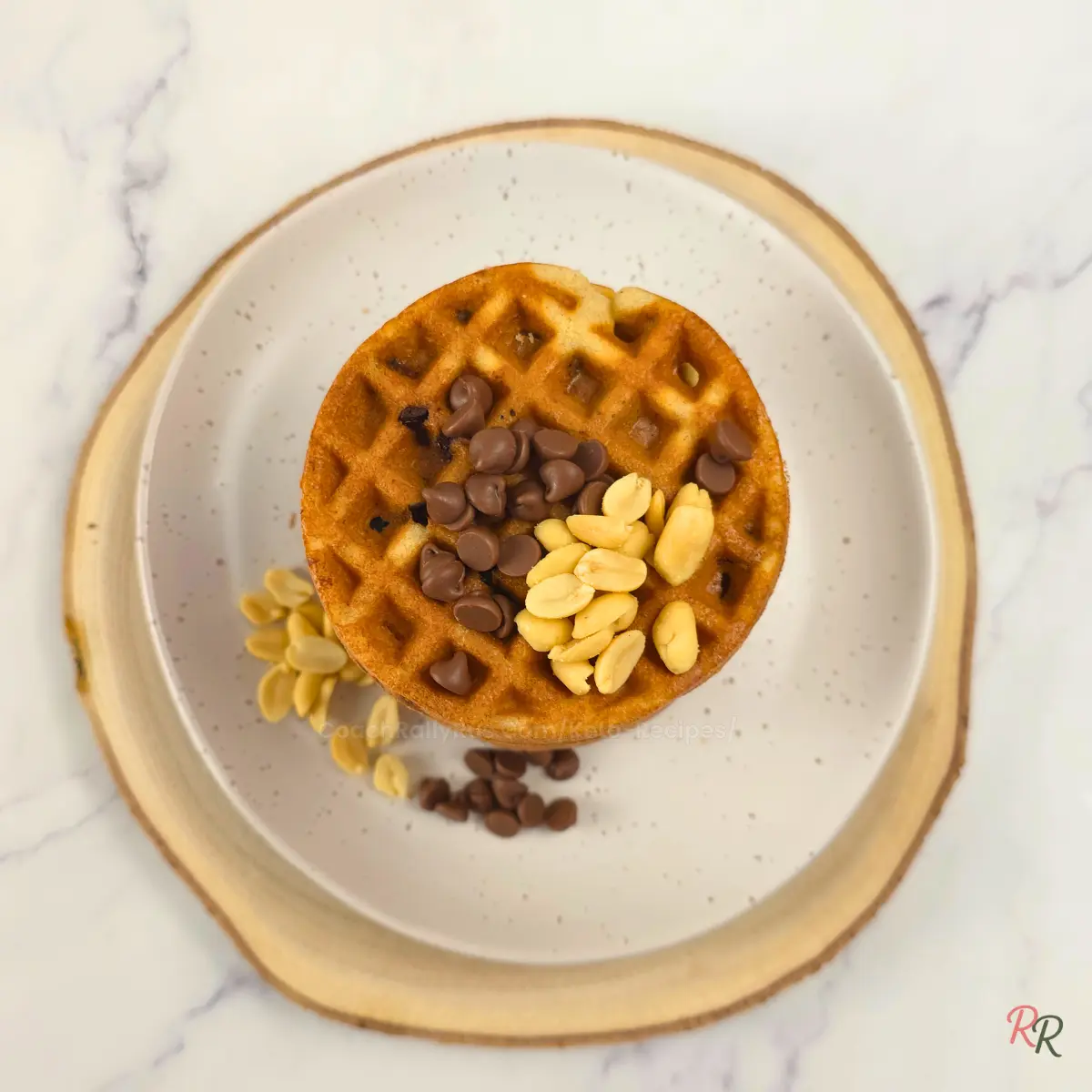 Overhead view of a single keto cookie waffle topped with chocolate chips and peanuts on a rustic plate by Rally Rus