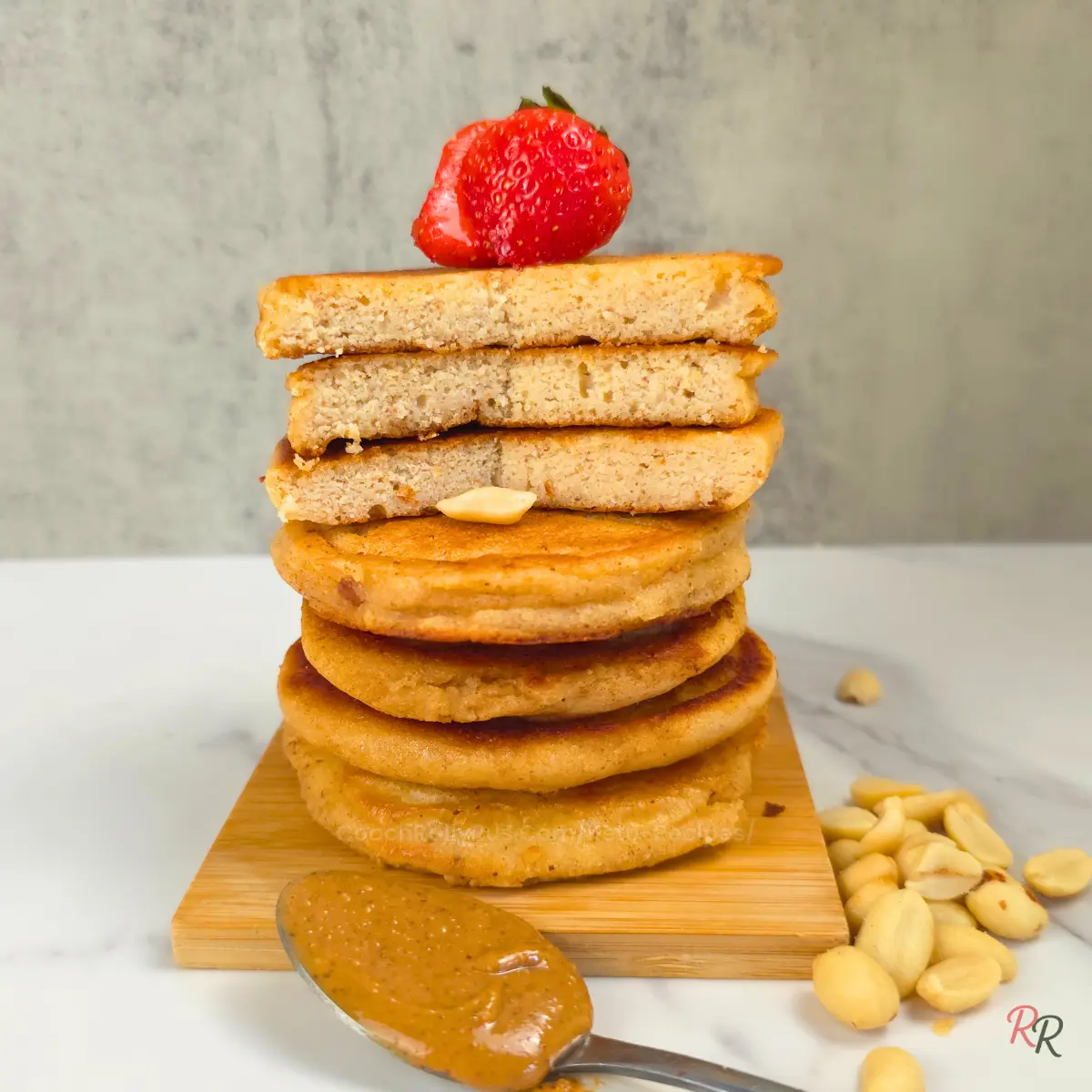 Stack of keto cottage cheese pancakes with a sliced peanut butter and jam pancake sandwich on top, garnished with a strawberry.