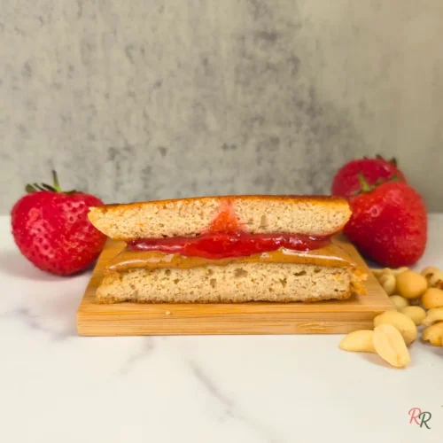 Close-up of a keto peanut butter and jelly pancake sandwich cut in half with strawberries and peanuts