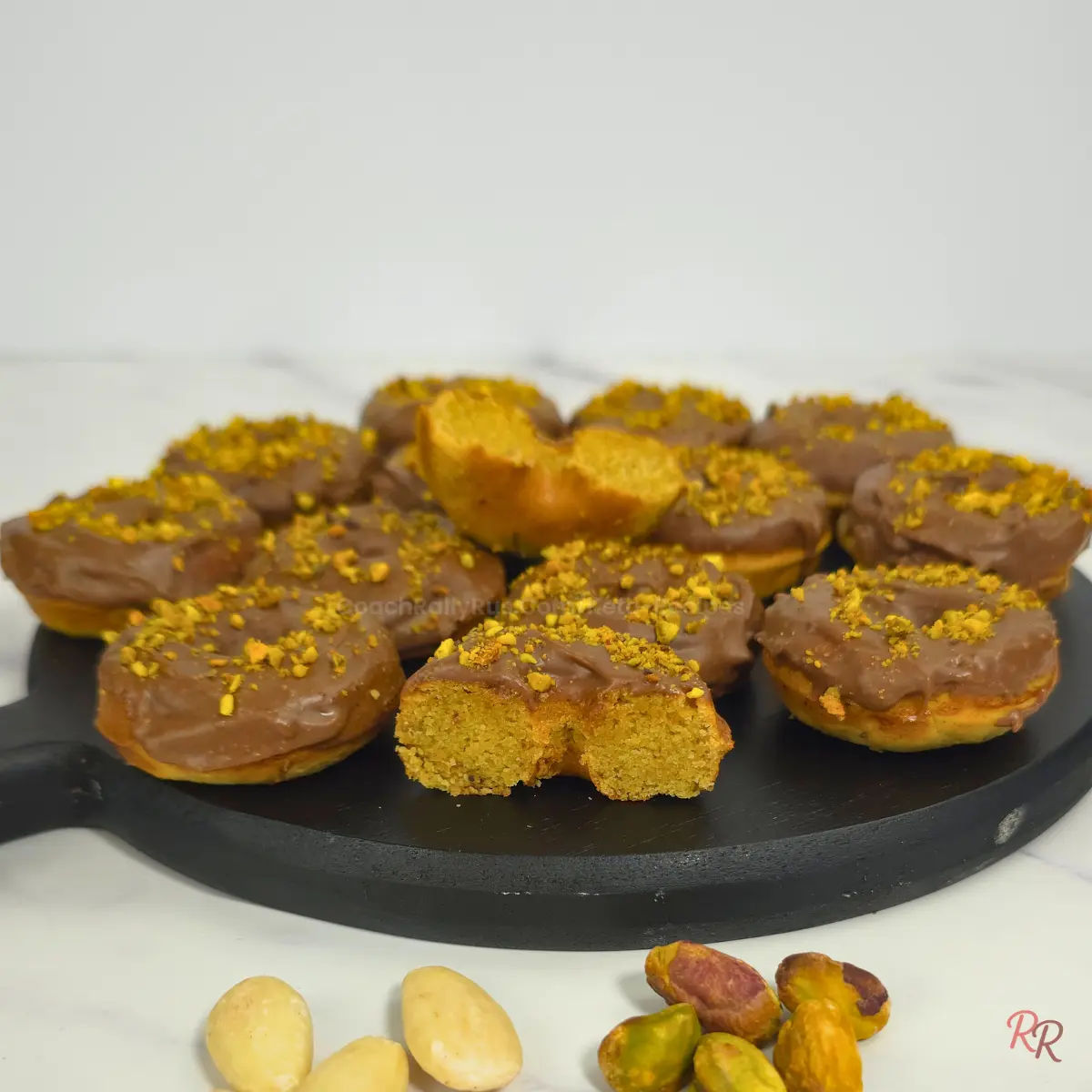 Glazed keto pistachio almond flour donuts with one donut sliced to show inside texture.