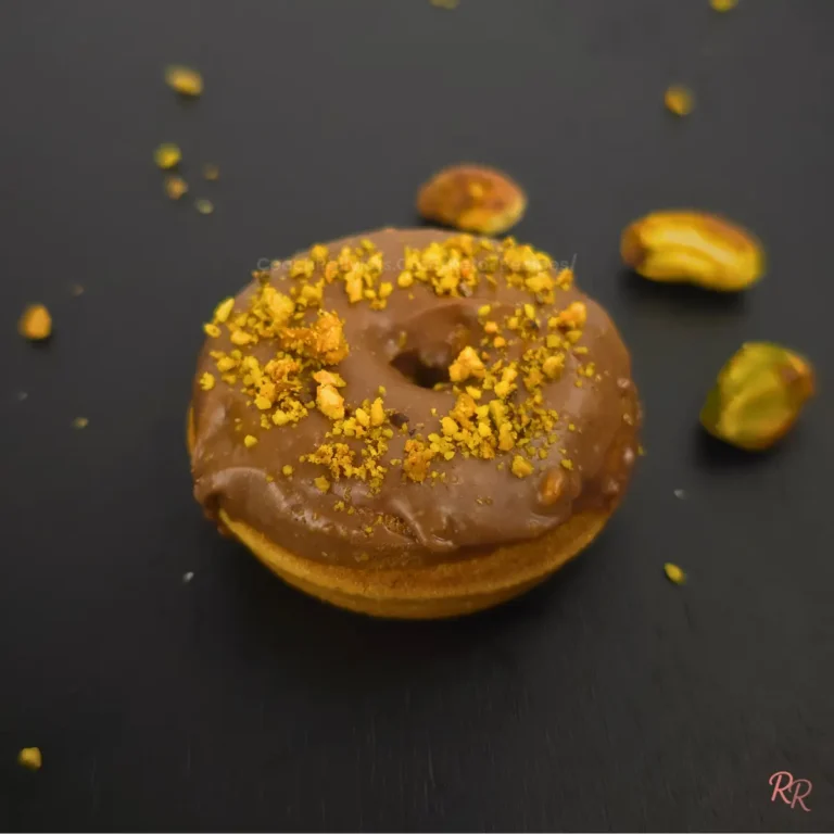 Keto pistachio cottage cheese donut with almond flour and chocolate glaze, topped with crushed pistachios.