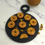 Overhead view of keto pistachio donuts with chocolate glaze and pistachio crumble, one with a bite
