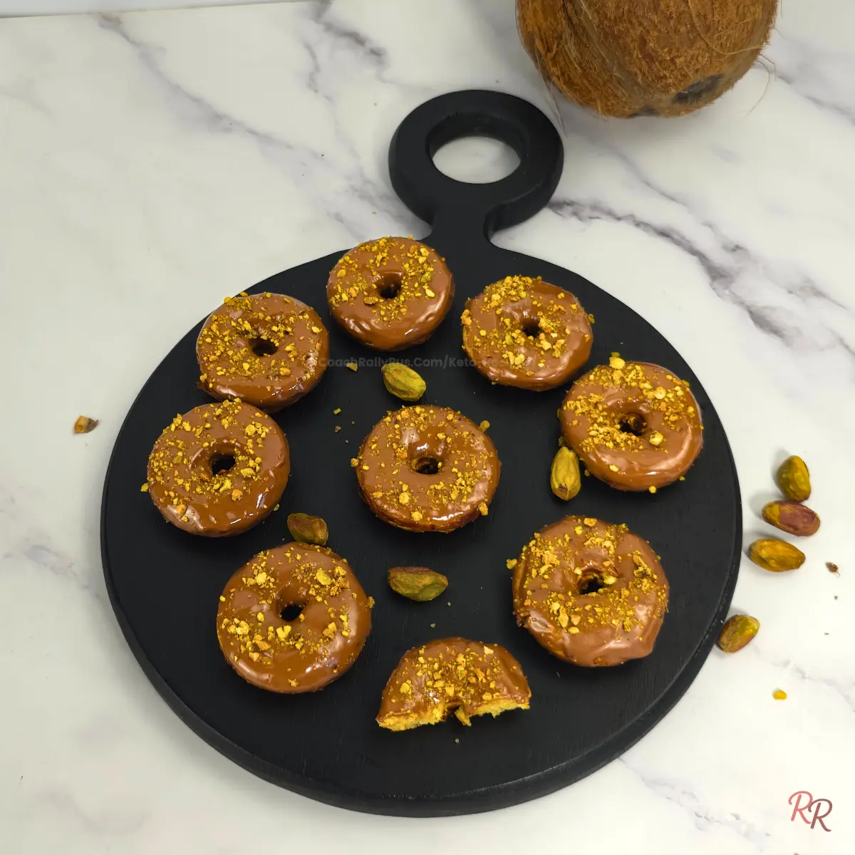 Overhead view of keto pistachio donuts with chocolate glaze and pistachio crumble, one with a bite