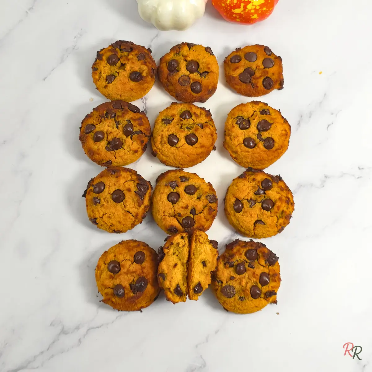 Pumpkin chocolate chip cookies arranged in rows with pumpkins