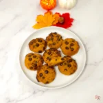 Keto pumpkin chocolate chip cottage cheese cookies on a white plate with autumn leaves and mini pumpkins