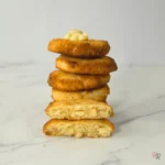 Keto white chocolate macadamia cookies stacked with chewy centers and crisp golden edges.
