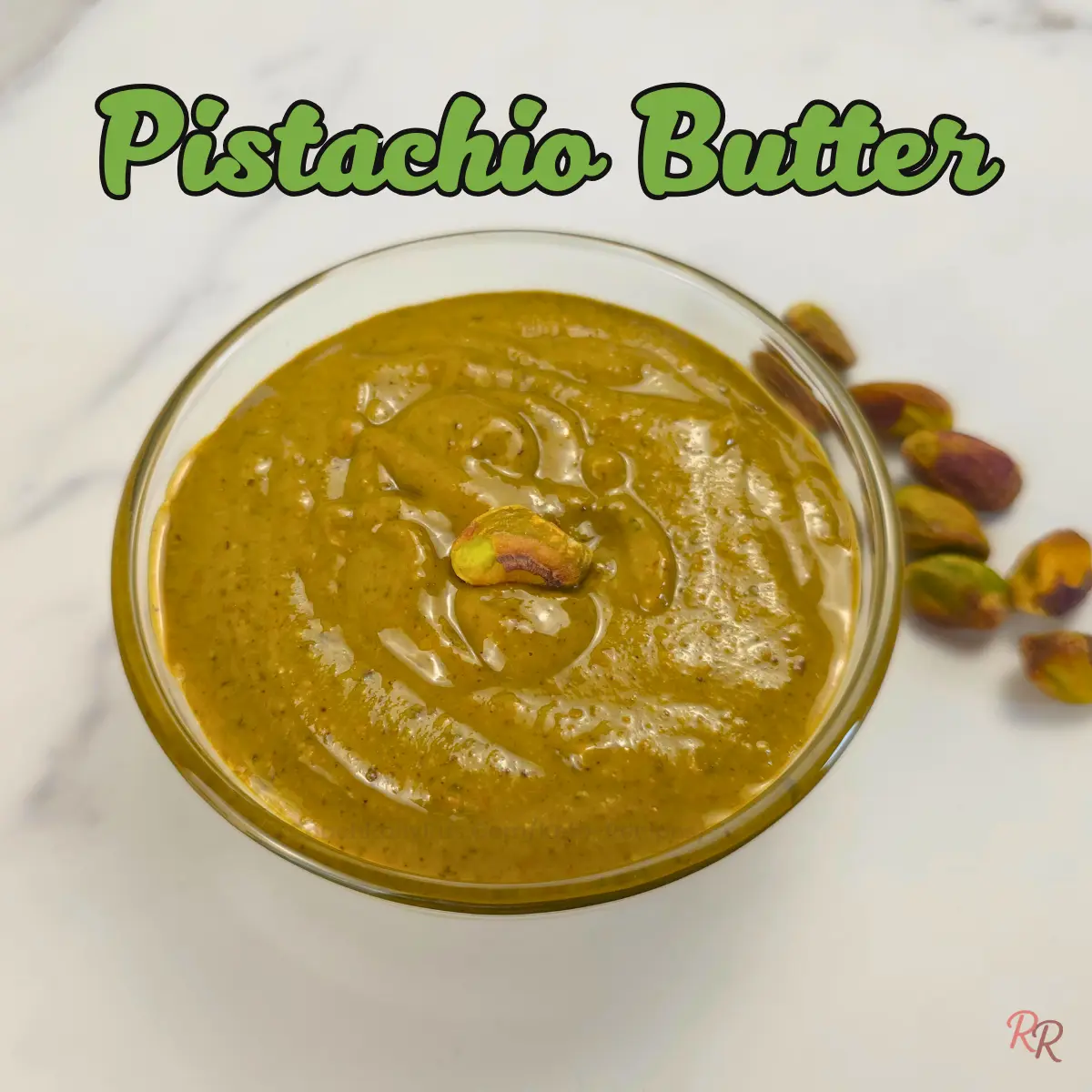Creamy homemade pistachio butter in a glass bowl with whole pistachios on the side