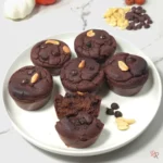 White plate of six keto chocolate muffins with peanuts and one muffin cut open to show rich interior.