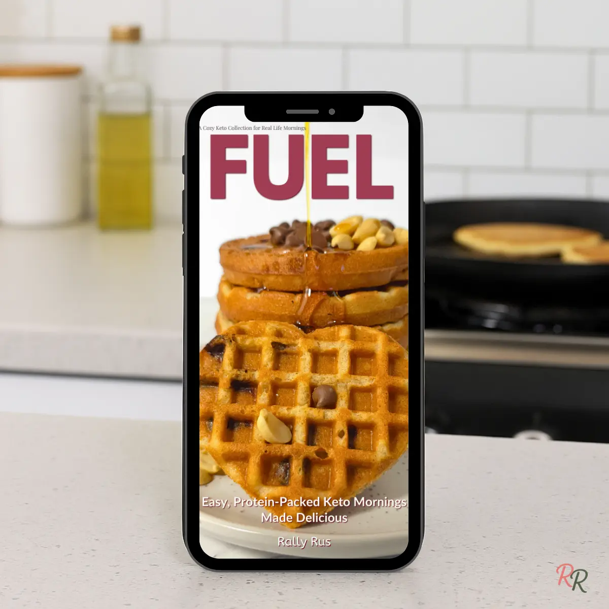 Fuel - Easy Protein-Packed Keto Breakfast eBook Phone displaying Fuel keto breakfast ebook on kitchen counter with pancakes in background