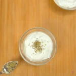 bowl of whipped cottage cheese dip with rosemary on top, placed on a wooden background