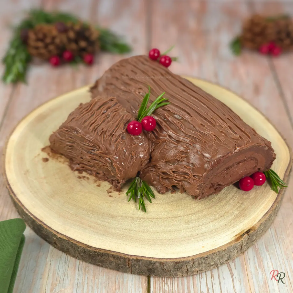 Close-up of a chocolate yule log cake with bark-textured frosting and red berries.