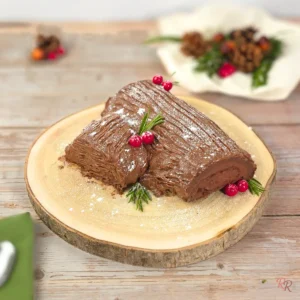 Keto chocolate yule log cake on wooden slab, dusted with powdered sweetener and decorated with cranberries and rosemary.