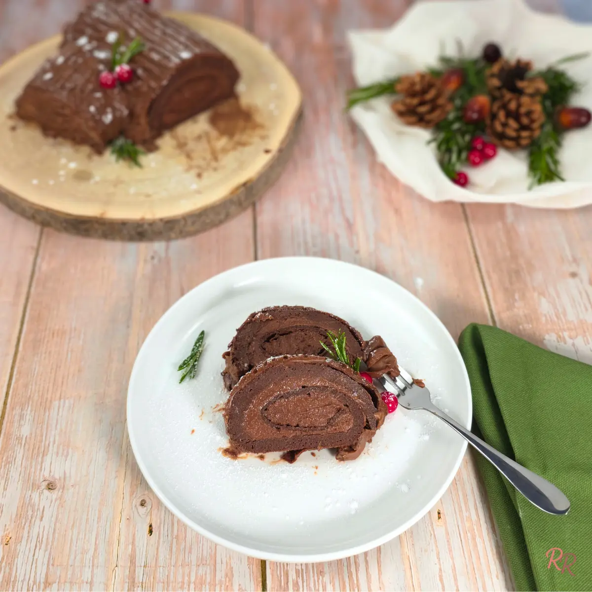 Two slices of keto yule log cake on a white plate with the full cake in the background.