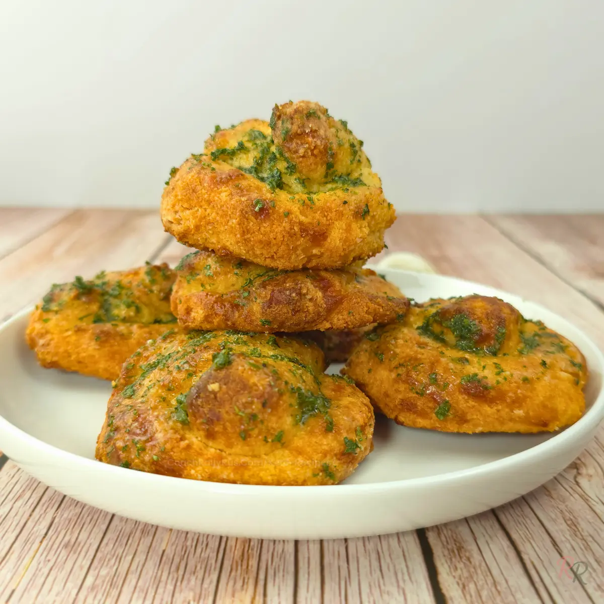 Stack of keto cottage cheese garlic knots on a white plate over rustic wood background.