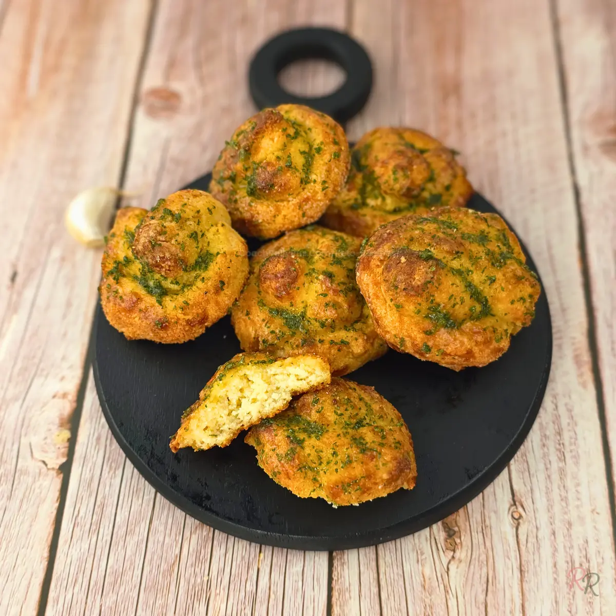 Garlic butter keto knots arranged on a black round board with rustic wood background and garlic clove.