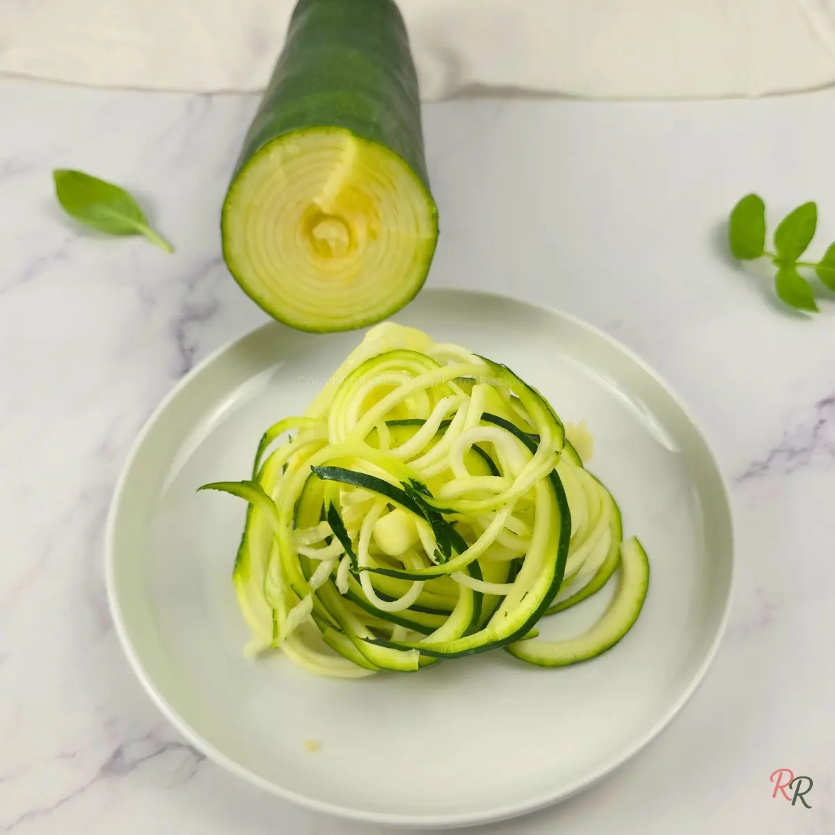 Raw Zoodles Fresh zucchini noodles on a white plate with spiralized raw zucchini and basil