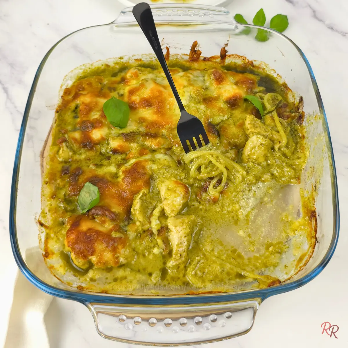 Zoodle Twirl in Creamy Pesto Chicken Casserole Fork twirling zucchini noodles in a half-eaten keto pesto chicken casserole with melted cheese and basil