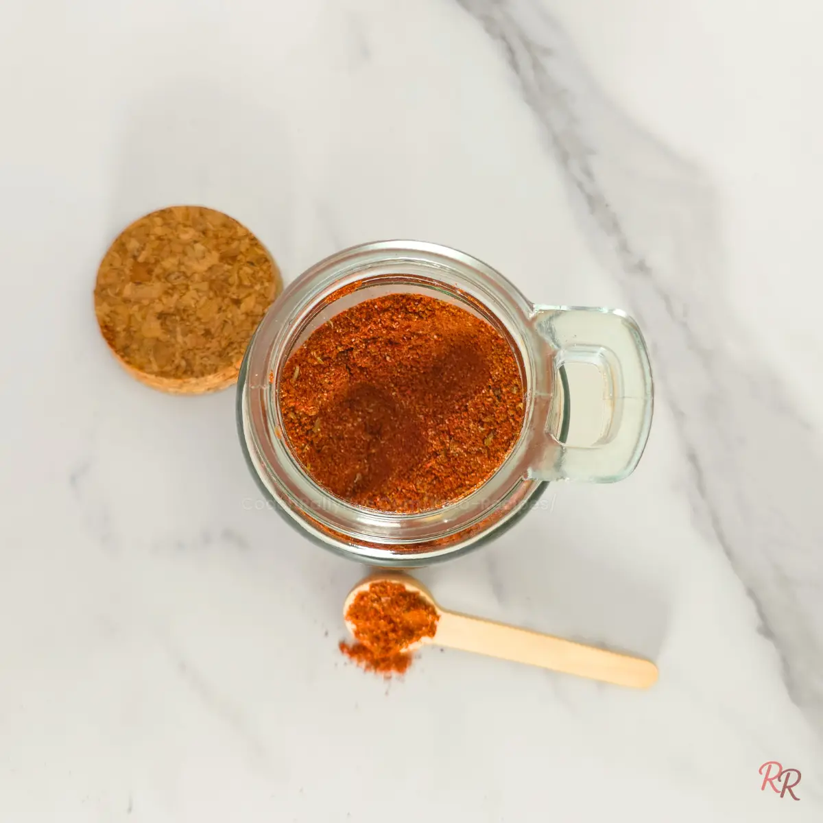 Open spice jar with taco seasoning on white marble.