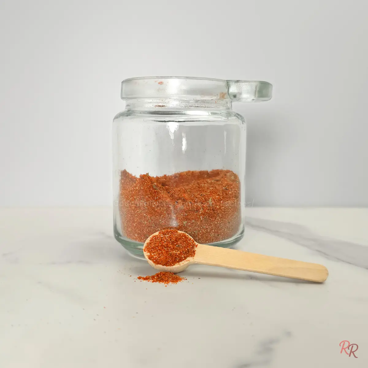 Taco seasoning in glass jar with wooden spoon on marble.